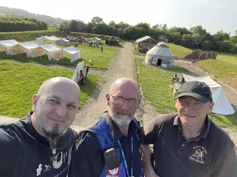 Three Society members at the entrance to the encampment, tents and a yurt on the slope behind them