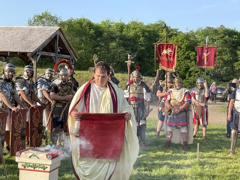Roman legionaries drawn up in formation behind a figure in a toga holding a red scroll