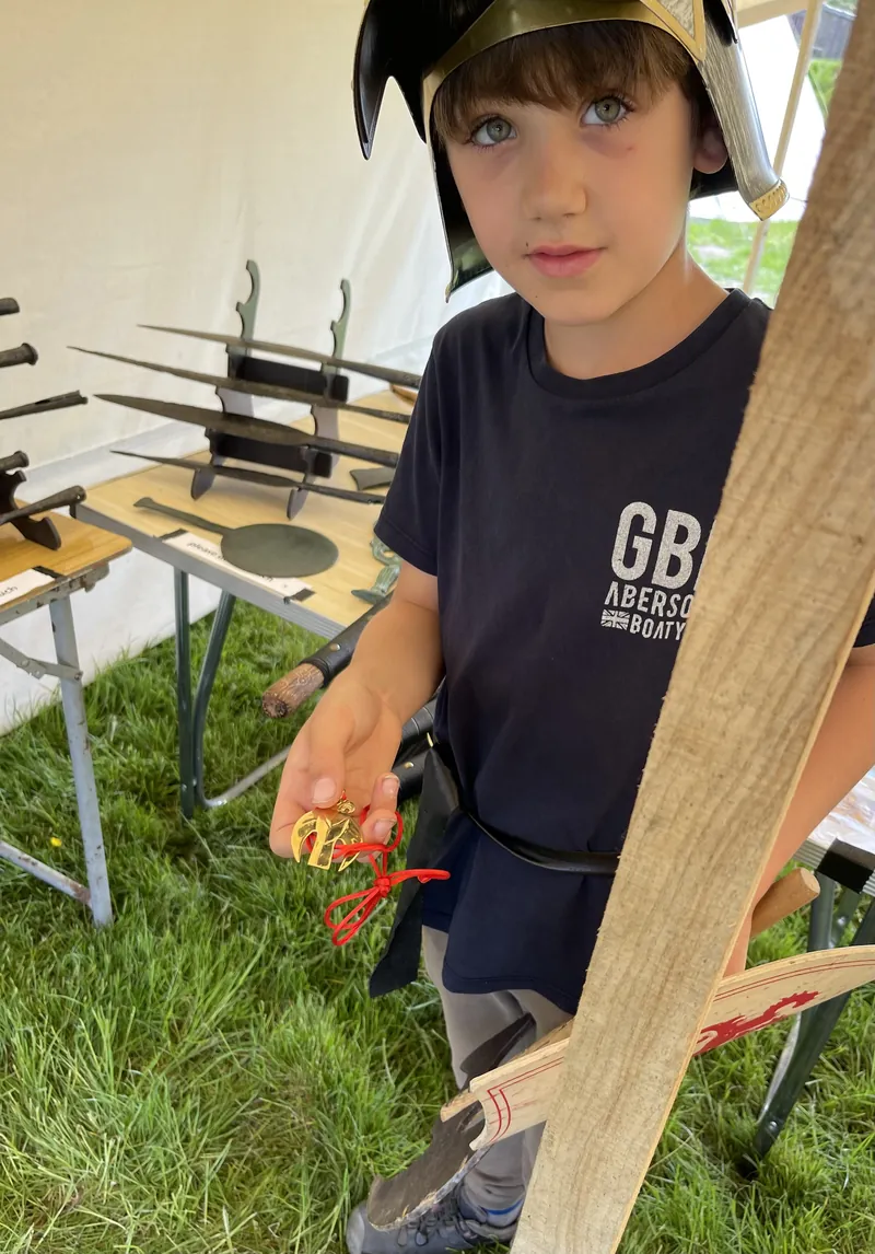 A boy wearing a Roman helmet at the Society's table, holding a wooden shaft