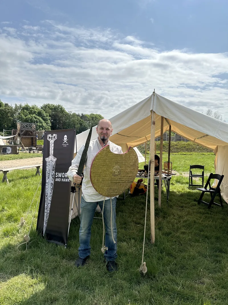 A Society member holding a round shield and sword beside the display banners