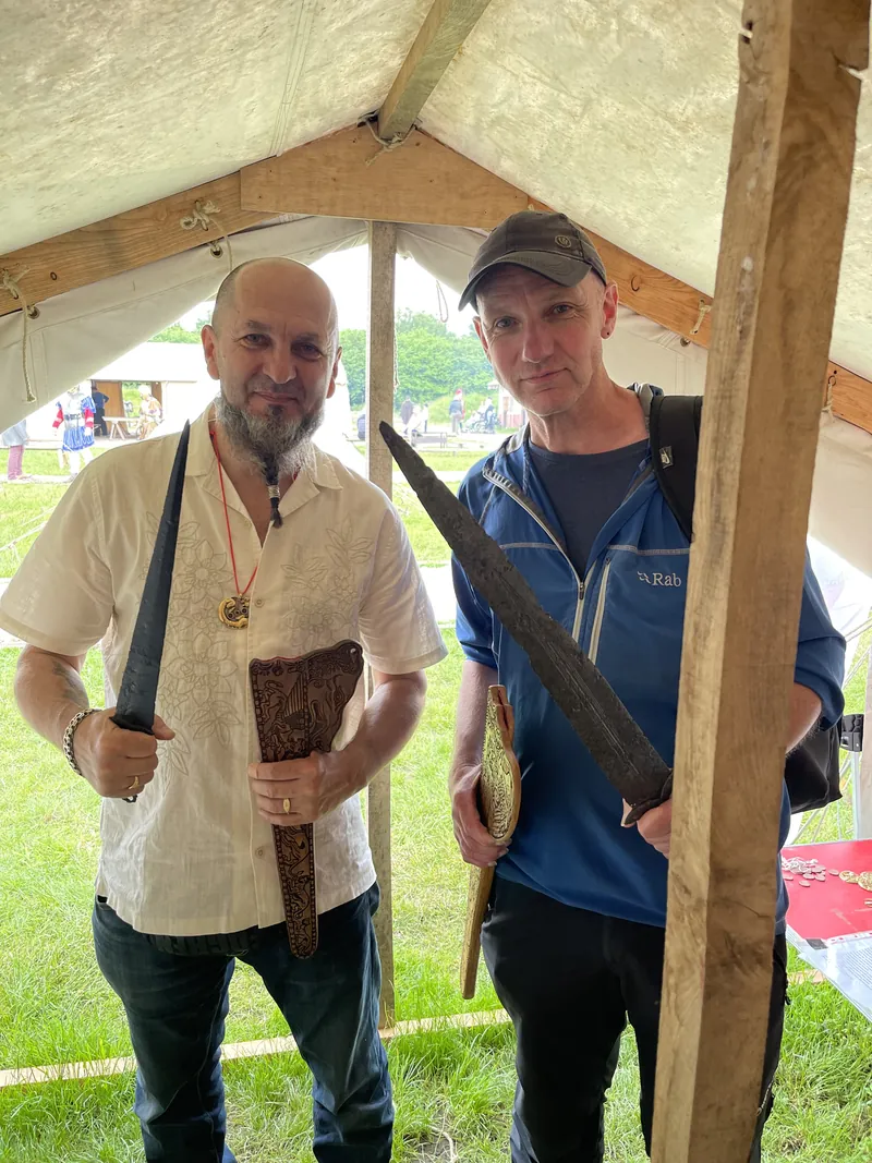 Two men at the display holding a long sword and a broad single-edged blade