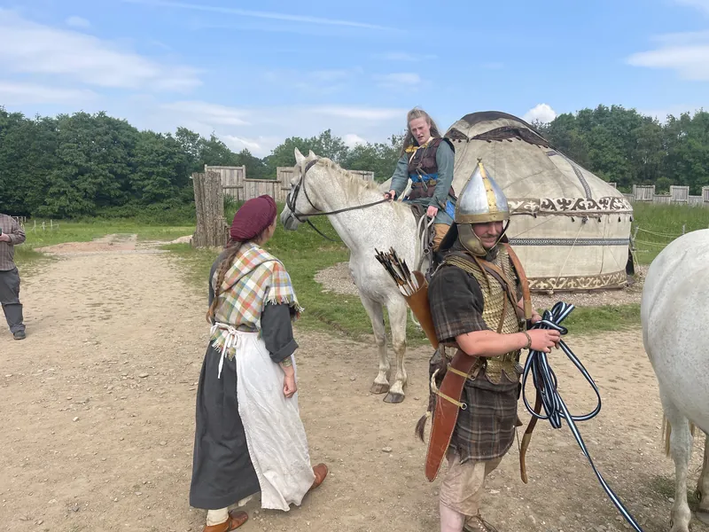 A rider leads a grey horse past the yurt while a companion walks alongside