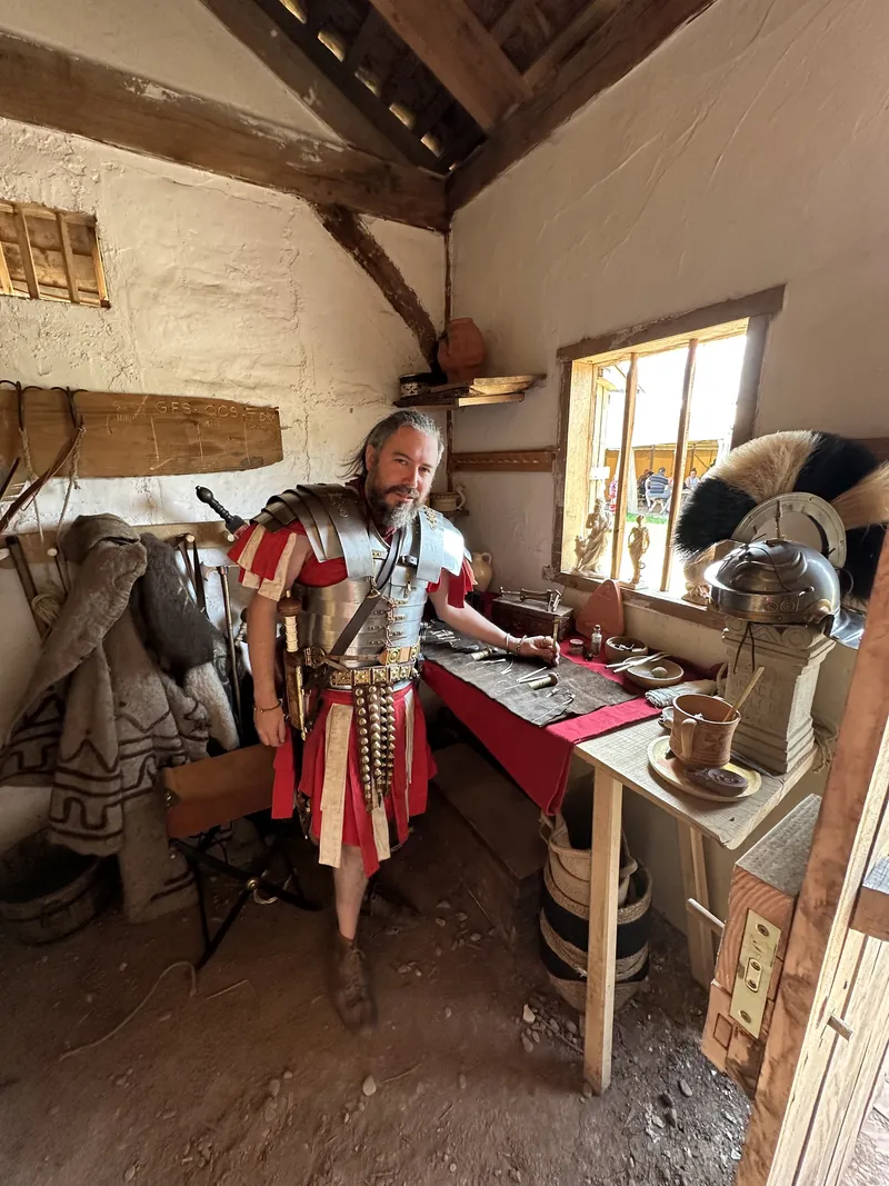 A re-enactor in Roman armour at a table of helmets and equipment