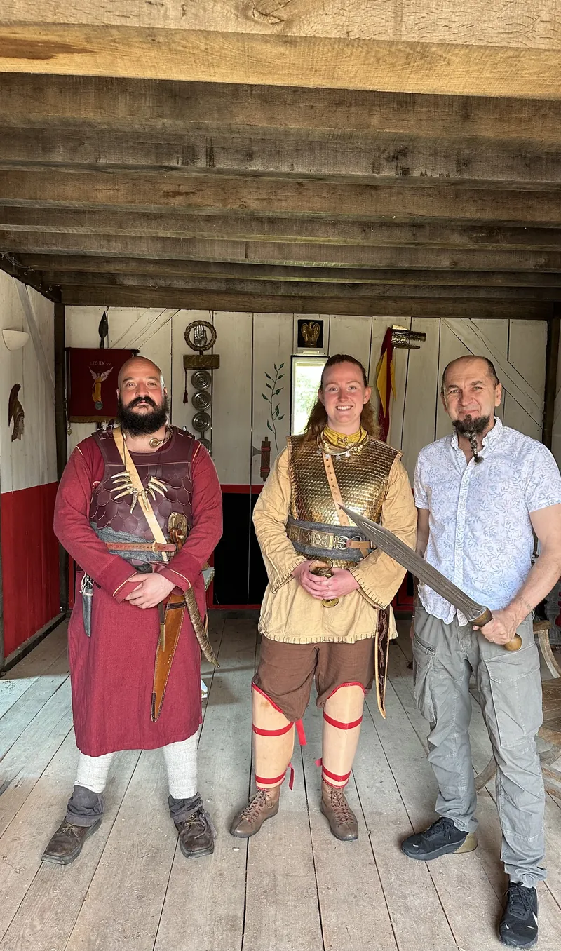Three people in reconstructed dress in the timber hall, one holding a sword
