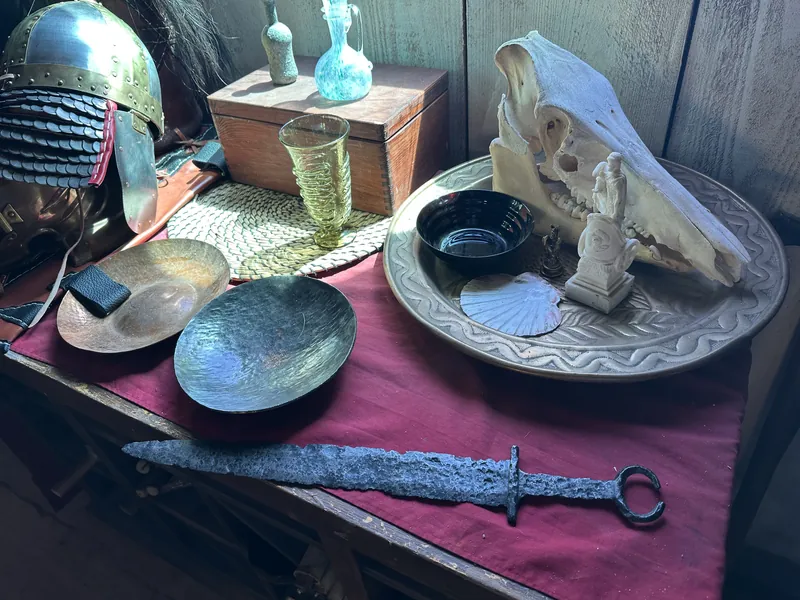 Helmet, glass vessels, silver dishes, an animal skull and an iron sword arranged on red cloth