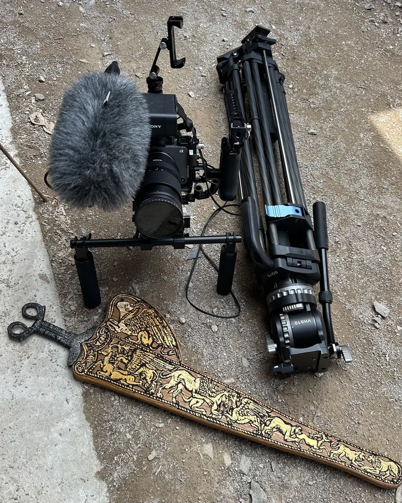 A gilded scabbard on the ground beside a film camera and tripod