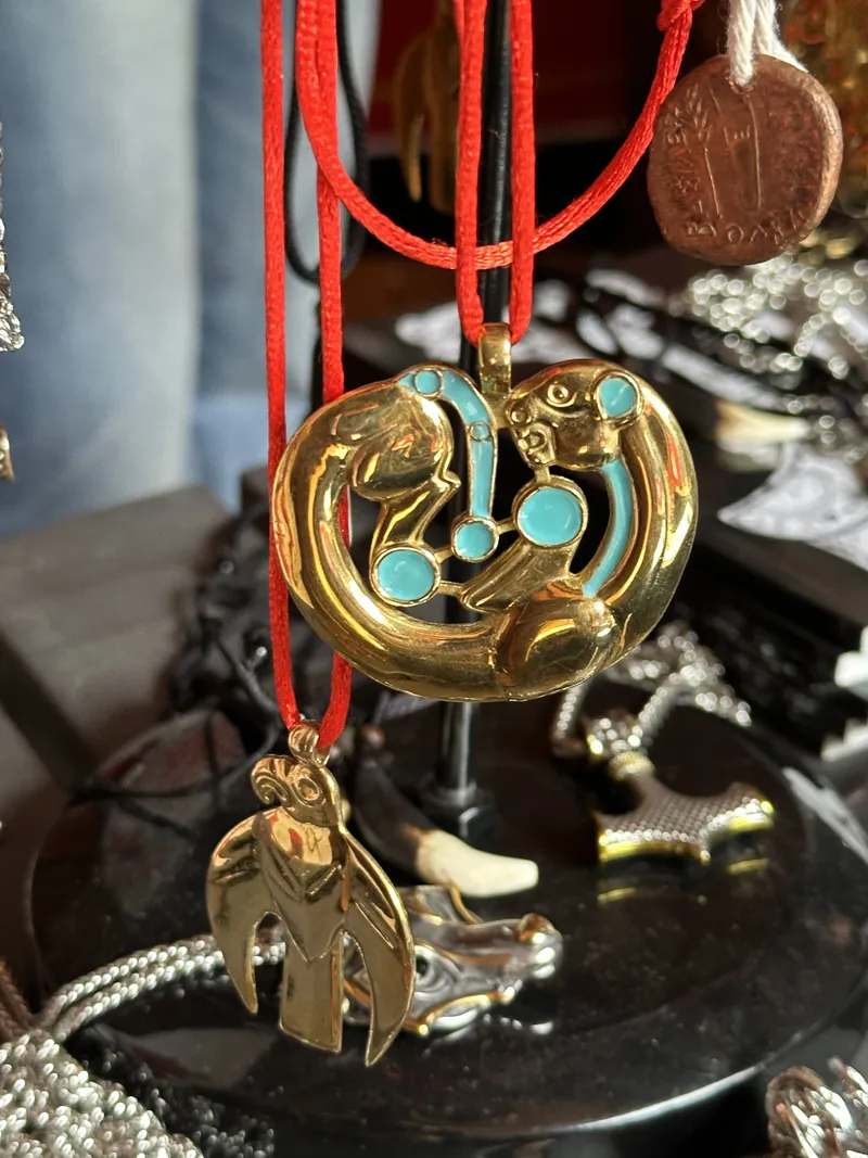 A gold pendant set with turquoise hanging on a red cord above the display