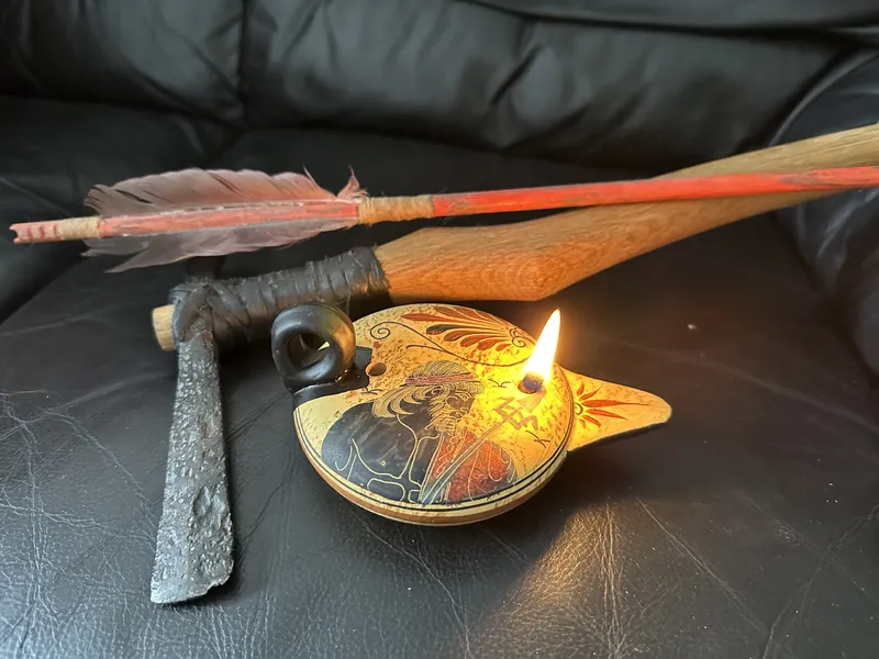 An arrow, an iron axe head and a lit oil lamp arranged together