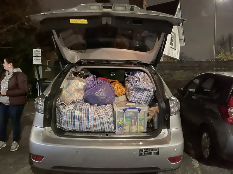 An estate car with its tailgate raised, packed to the roof lining with bags of clothing and boxes of food