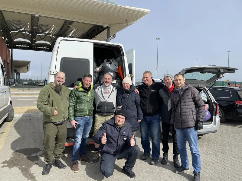 Volunteers gathered for a group photograph in front of the loaded vehicles at a service station