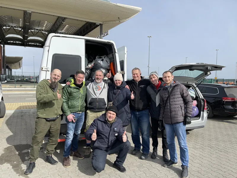 The same group of volunteers photographed from a lower angle, vans and cars behind them
