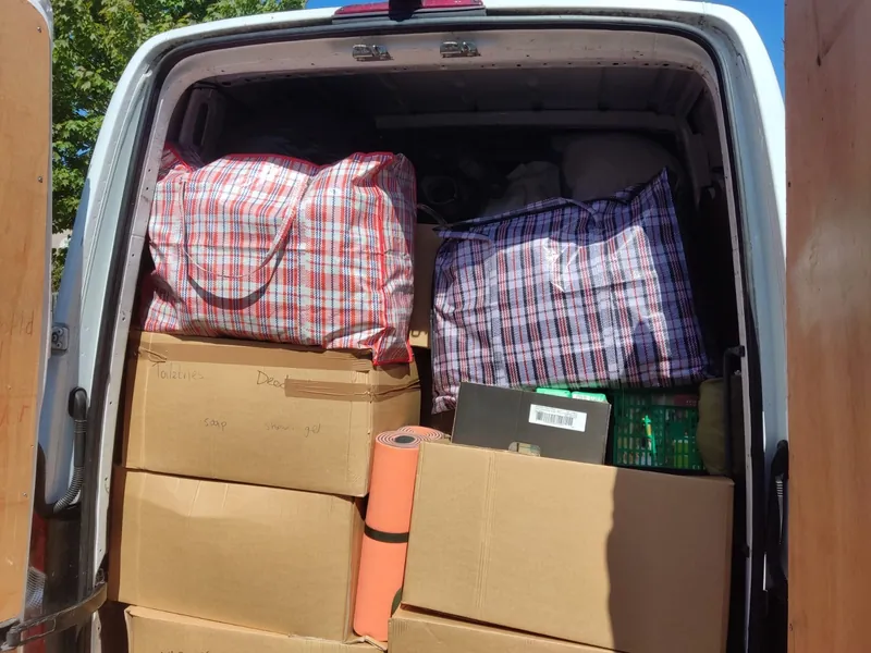 The inside of a van packed with checked laundry bags, cardboard boxes and rolled sleeping mats