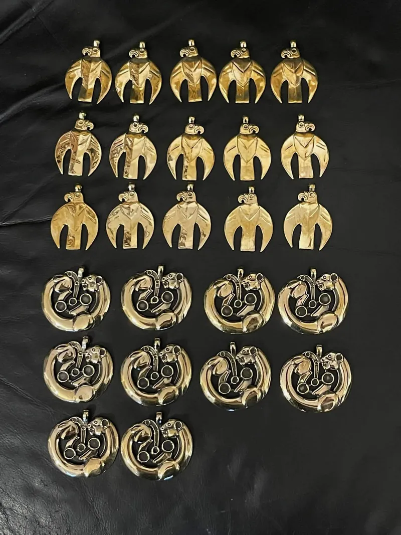 Rows of cast pendants on a dark surface: bird-form above, openwork roundels below