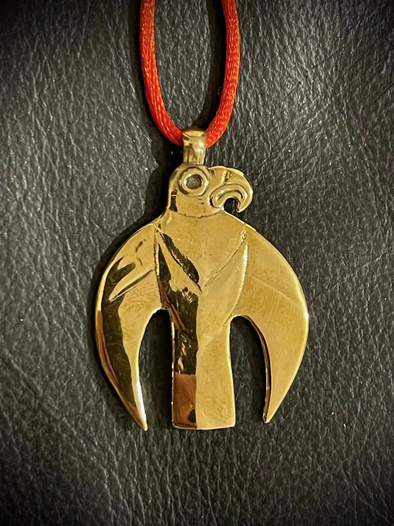 A pendant in the form of a bird of prey with folded wings, on a red cord